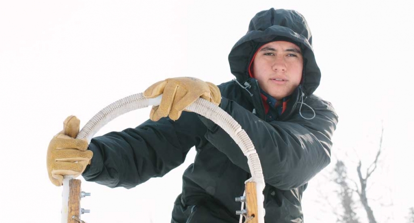 a person wearing snow gear holds the handles of a sled and looks at the camera